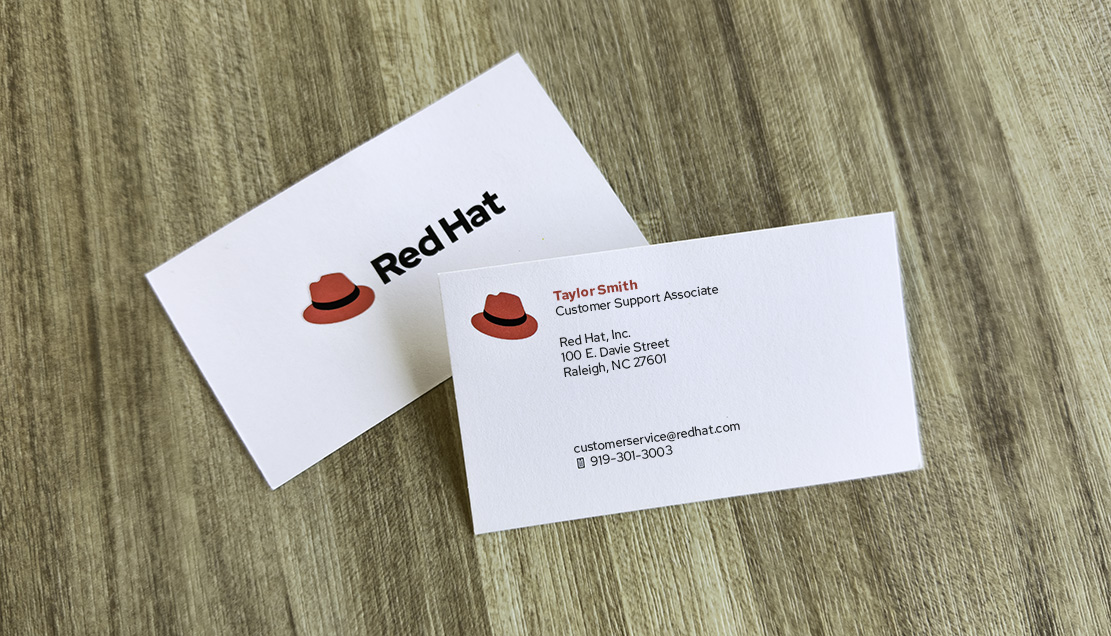 Red Hat の名刺の写真。Red Hat の社員の名前の横に帽子が描かれている。