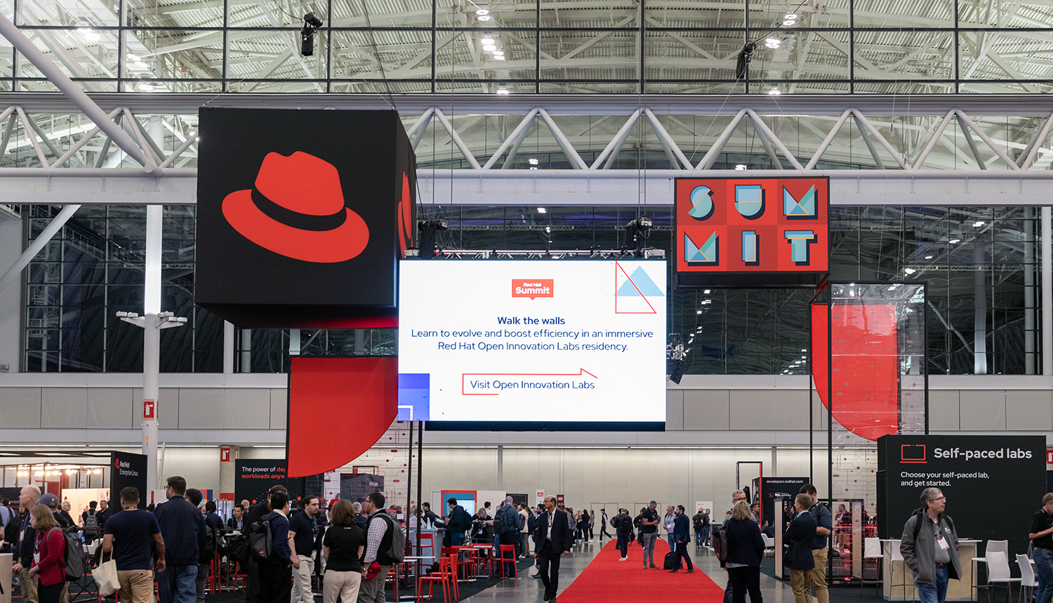 Red Hat Summit のエキスポホールでの写真。ブースの上に帽子の大きな看板がぶら下がっている。