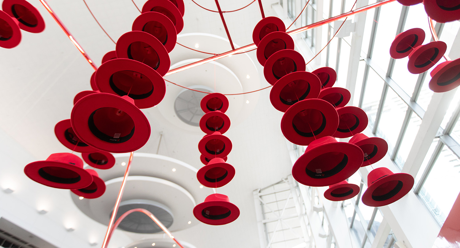 Red Hat Summit のディスプレイで、Red Hat Cool Stuff Store のブースの上に吊されている数十個のフェドラハット。