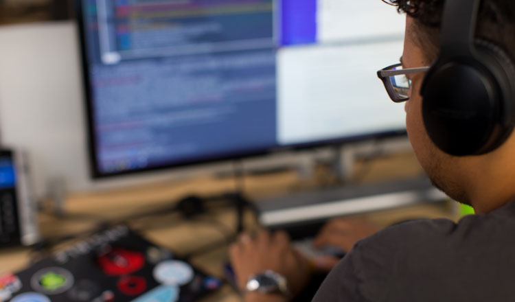 Um profissional da área tecnológica trabalha em uma mesa com monitores de computador