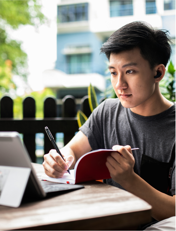 Foto di una persona che scrive su un quaderno mentre guarda un tablet